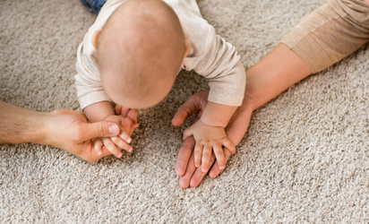 Baby holding parents hands on beige carpet