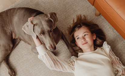 Girl and dog lying on beige carpet