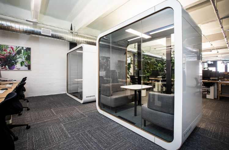 Office space with grey carpet and grey upholstered armchairs in clear working cubes
